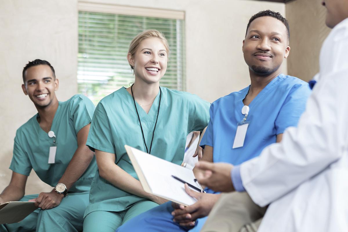 Three seated residents smile as they listen to an attending physician.